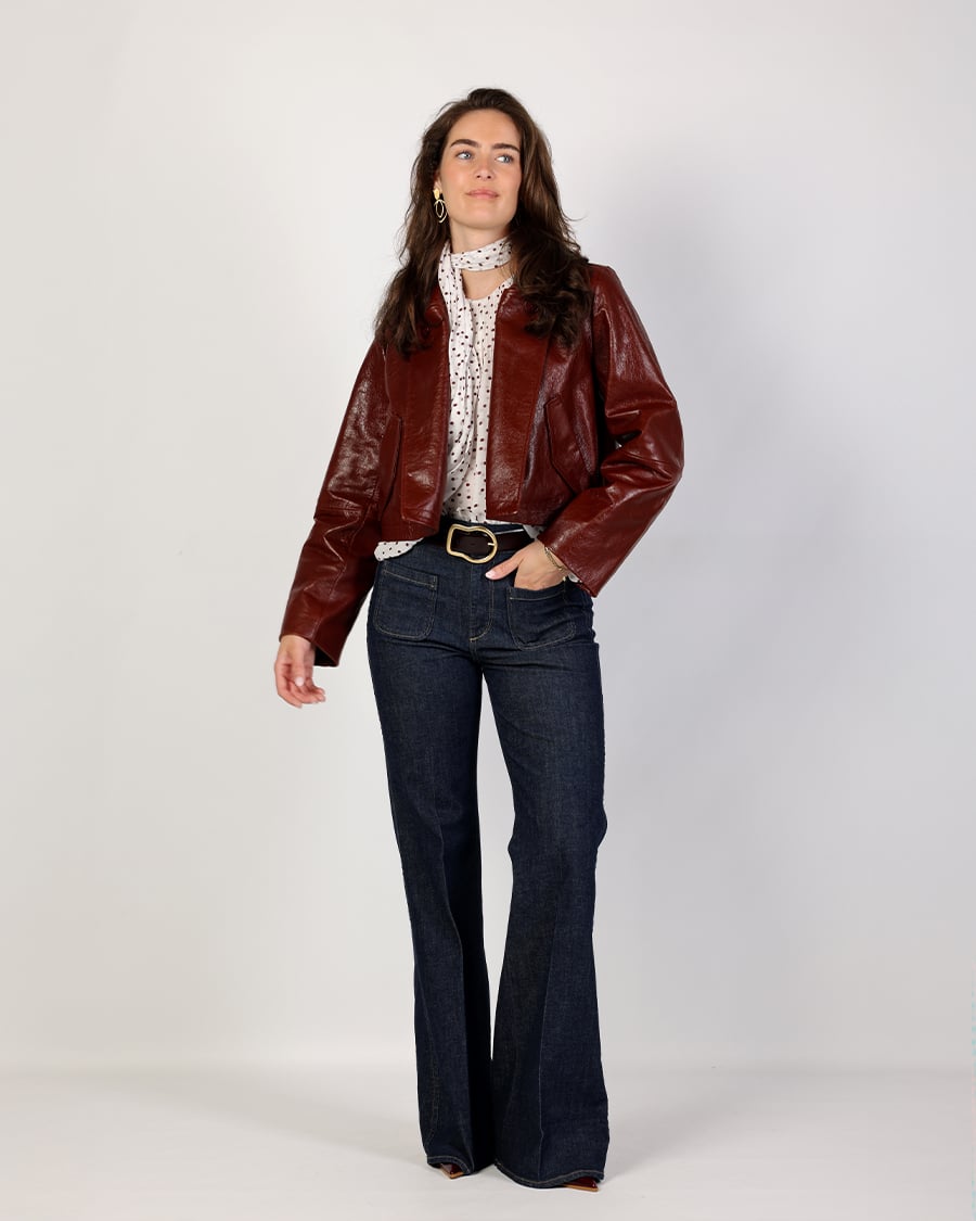 Dames outfit met bordeaux leren jas, donkere flared jeans en witte blouse met subtiele print