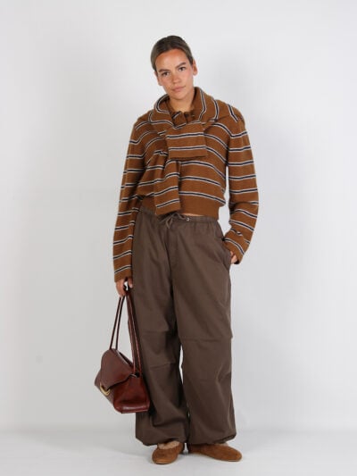 Frontale dameslook met bruin gestreepte trui, wijde broek en leren handtas